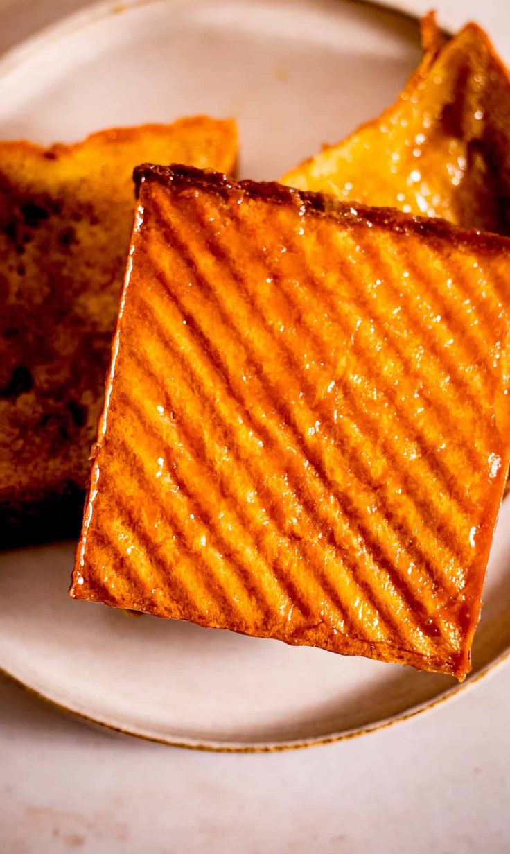 two pieces of grilled cheese sit on a plate next to another piece of bread