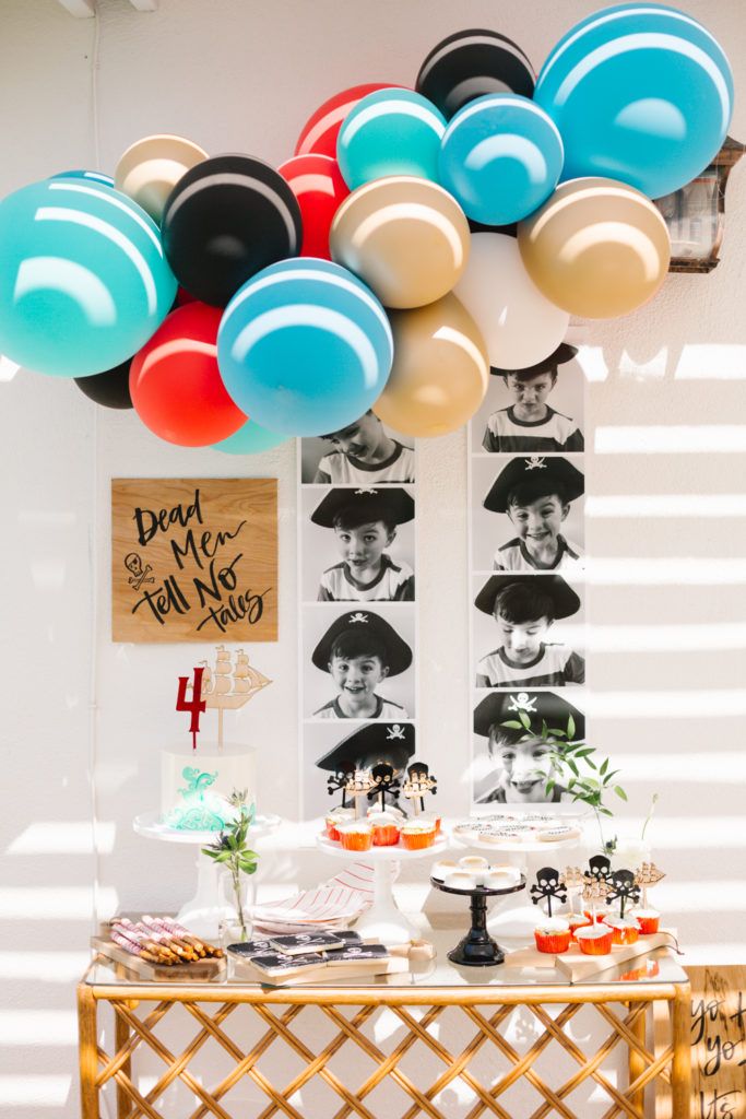 a table topped with lots of balloons next to a wall filled with pictures and desserts