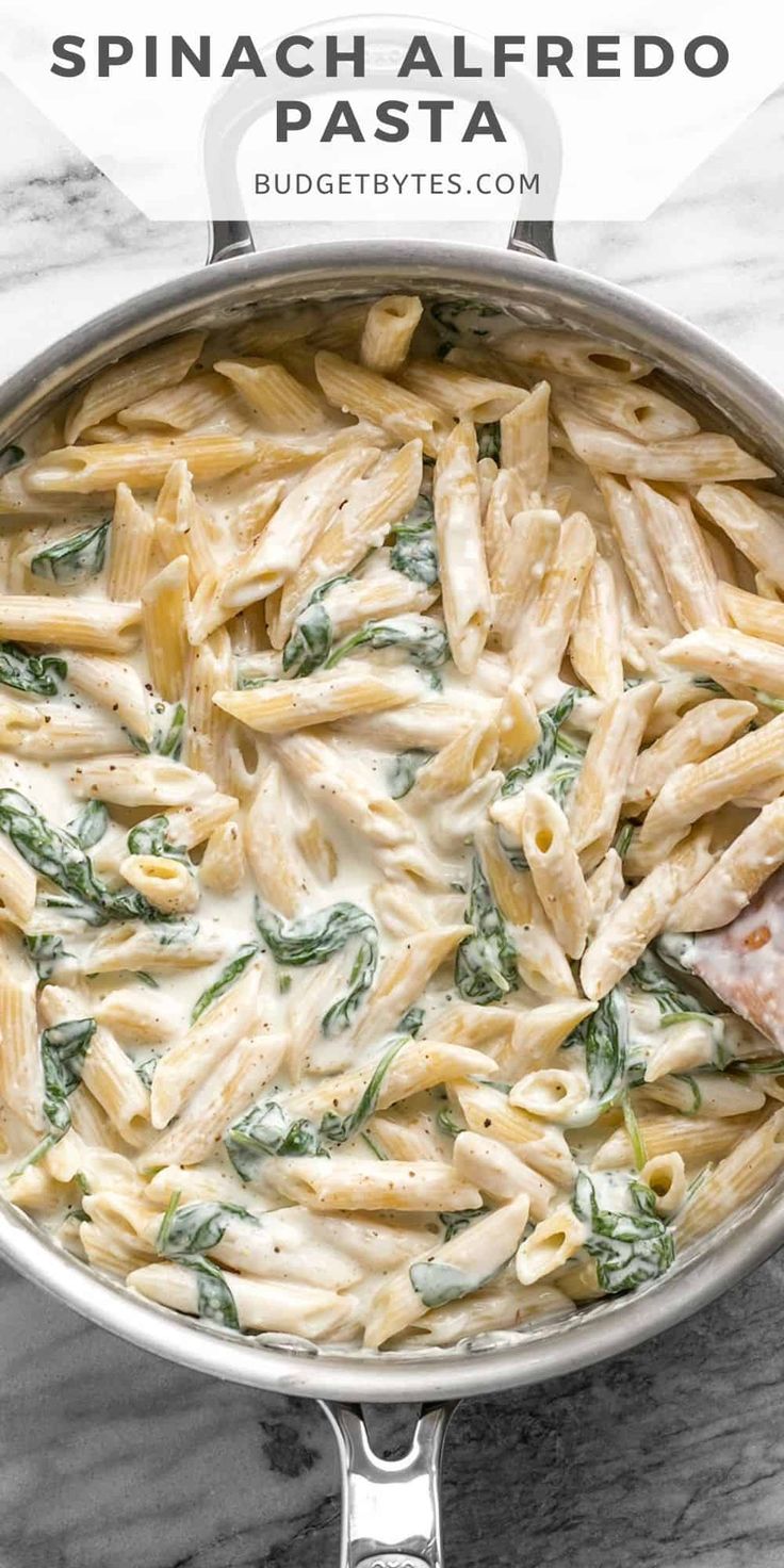 spinach alfredo pasta in a skillet on a marble counter with text overlay