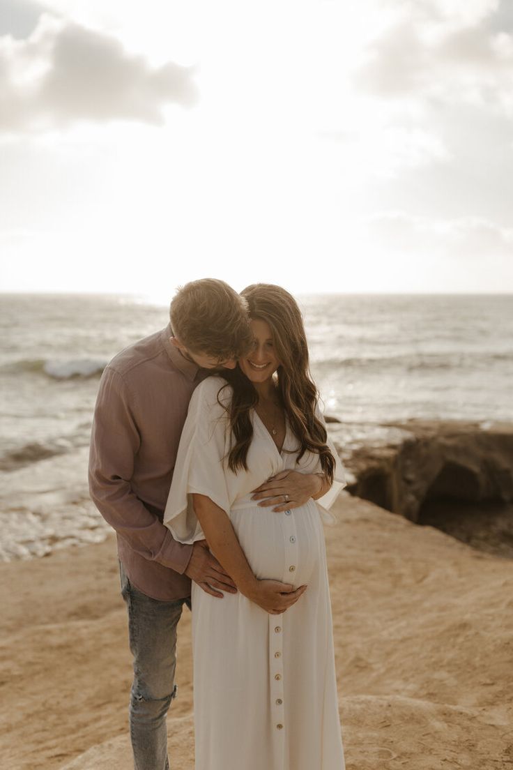 a pregnant couple embracing on the beach at sunset