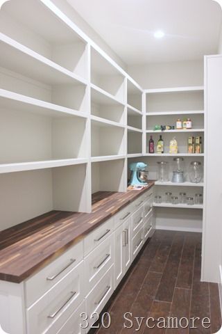 an empty walk in closet with white cabinets and wood counter tops on the bottom shelf