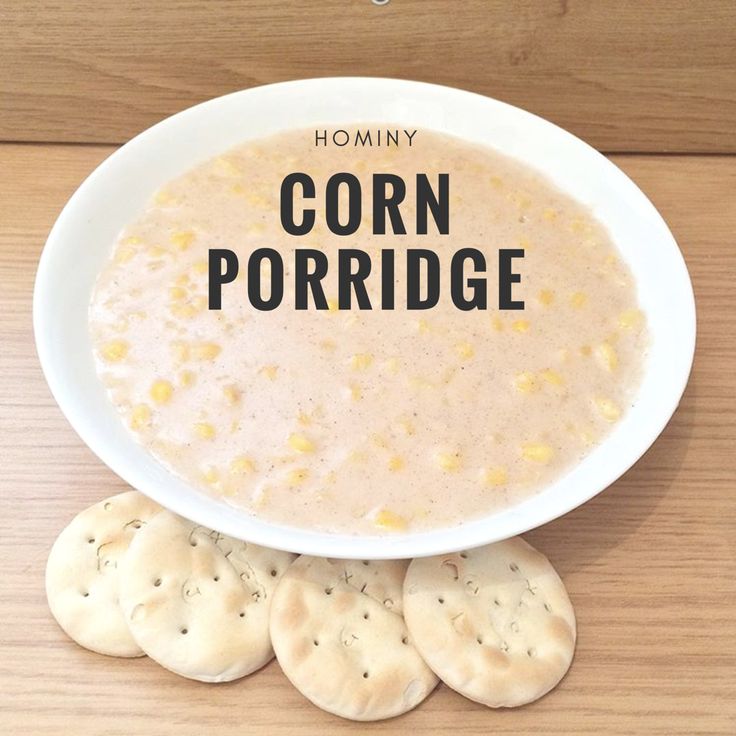 a white bowl filled with corn porridge next to crackers on a wooden table