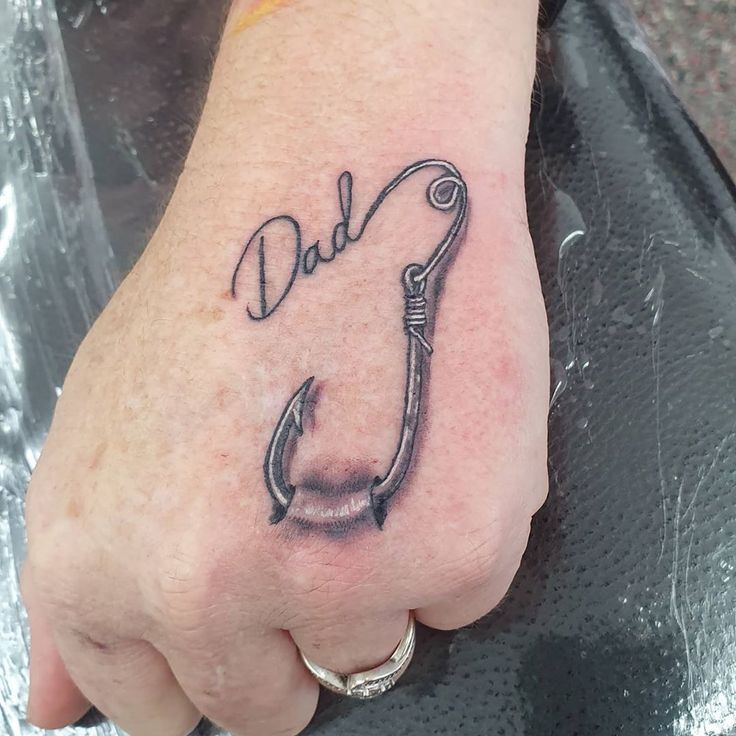 a man's foot with a fishing hook tattoo on it and the word dad written in cursive font