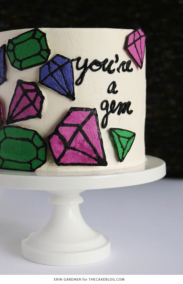 a white cake with pink and green icing decorated with colorful diamond shapes on it