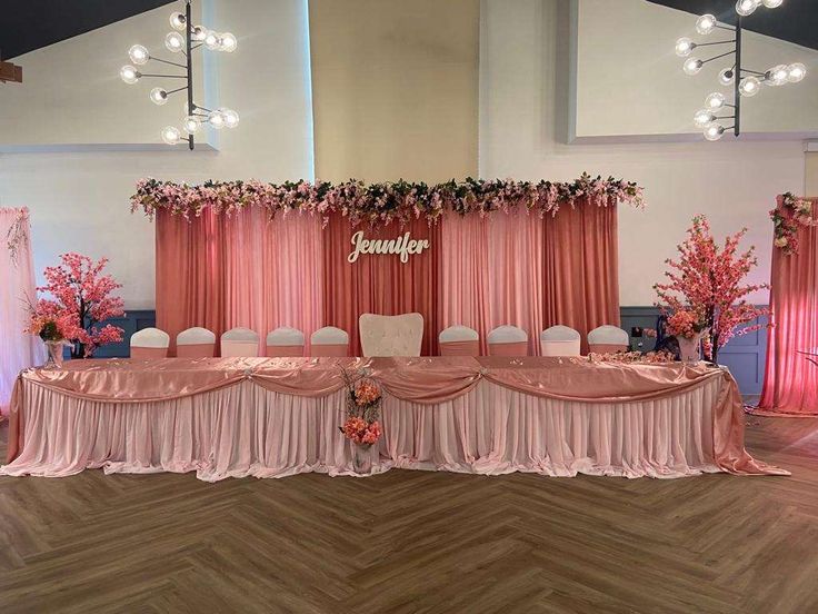 a banquet table set up with pink drapes and flowers on the back drop cloth