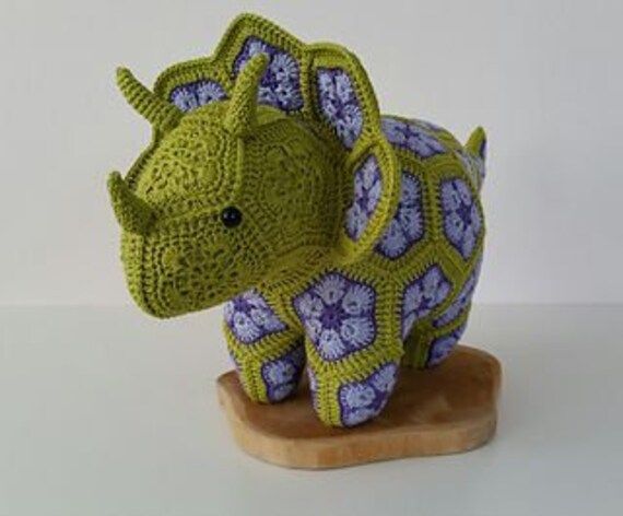 a crocheted rhinoceros sitting on top of a wooden base with purple and blue flowers