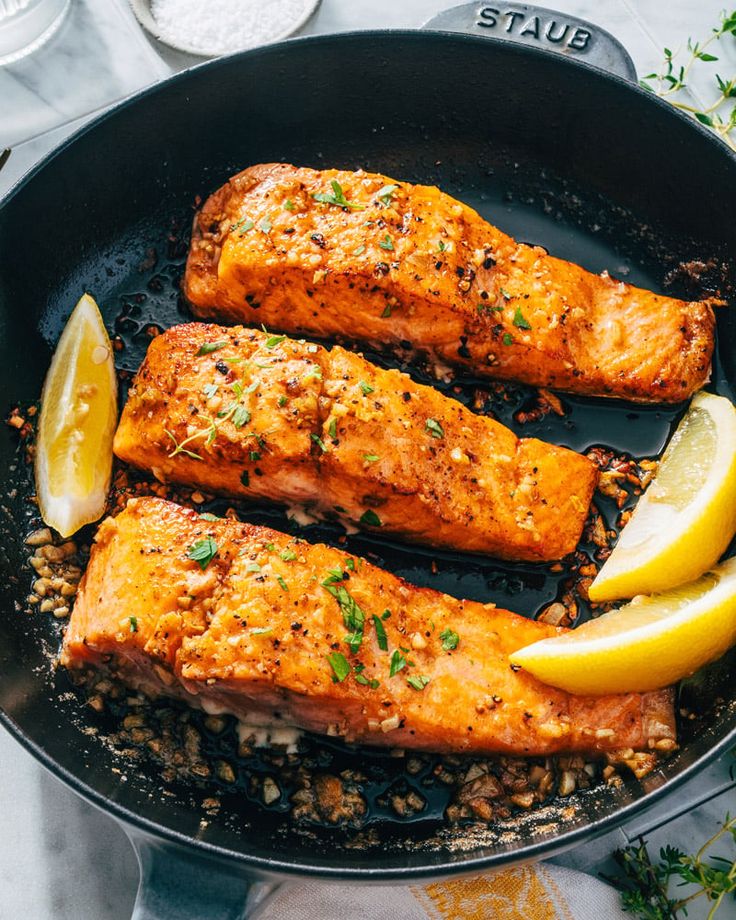 three salmon fillets in a skillet with lemon wedges