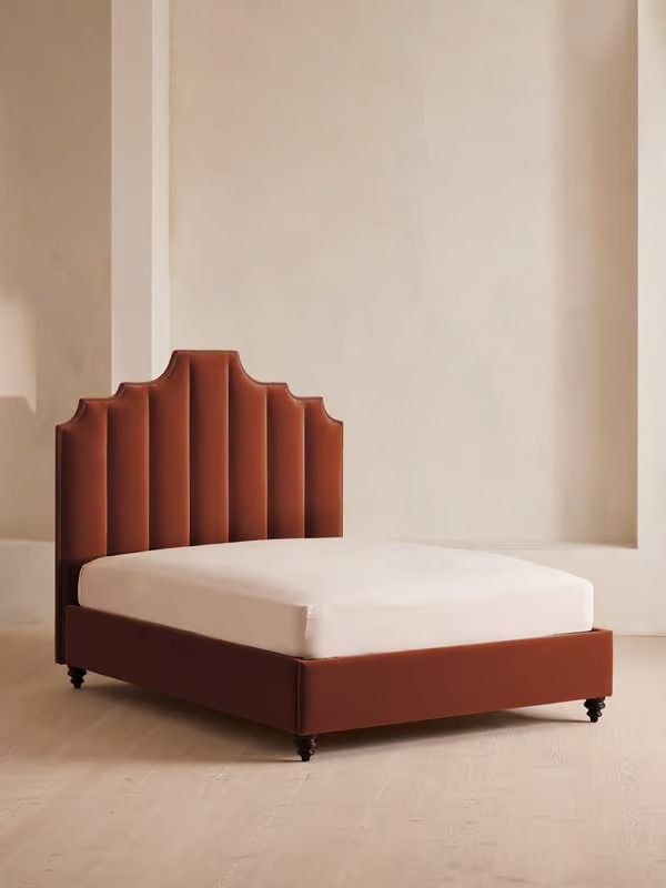 an upholstered bed with a white sheet and brown headboard in a room