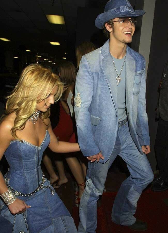 a man in a blue suit and cowboy hat walking next to a woman wearing jeans