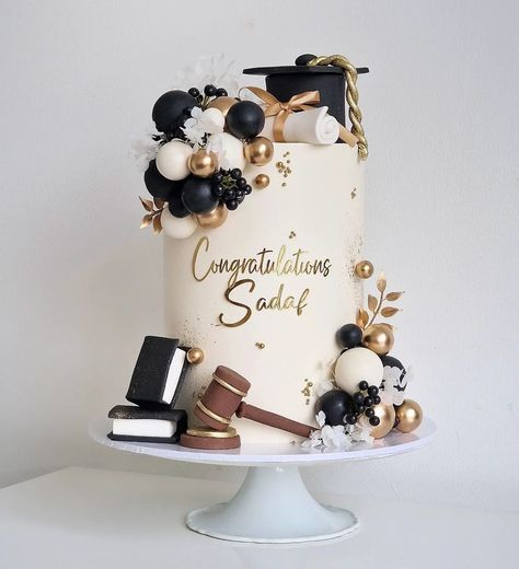 a graduation cake decorated with gold and black decorations on a white pedestal in front of a white wall