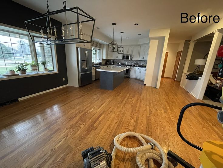 an empty living room with hard wood flooring and a vacuum in the foreground