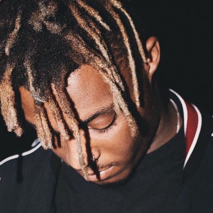 a man with dreadlocks looking down at his cell phone while wearing a black shirt