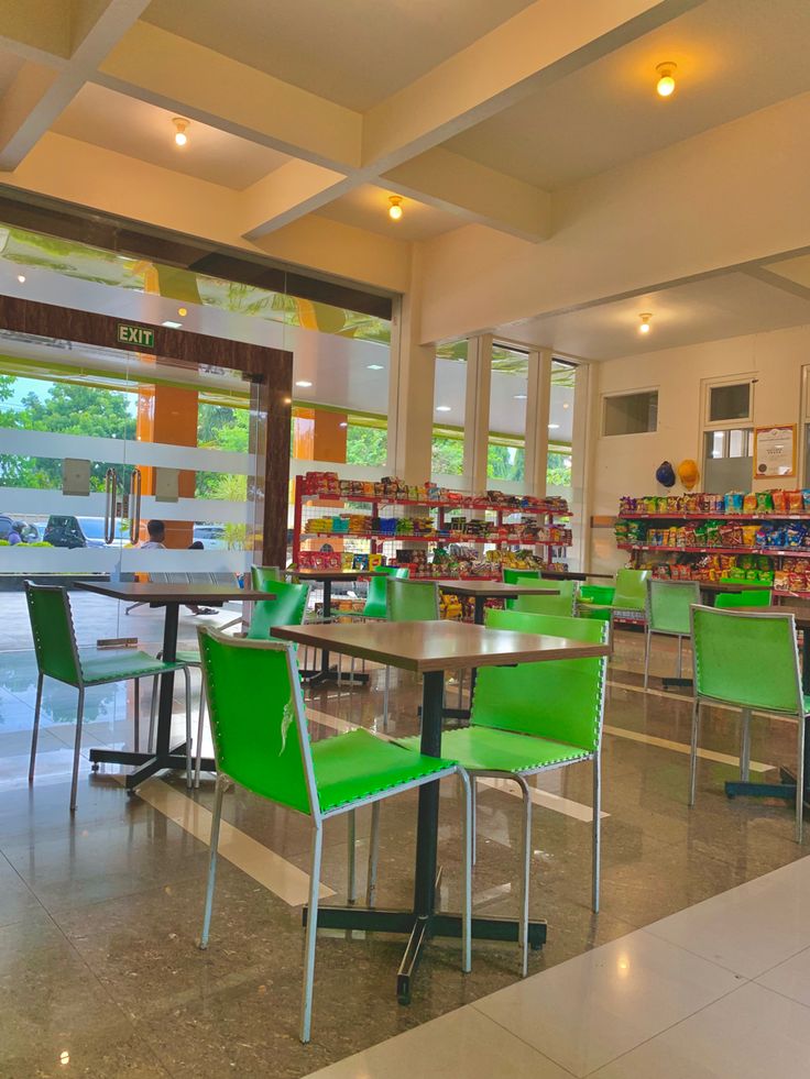 an empty cafeteria with tables and green chairs