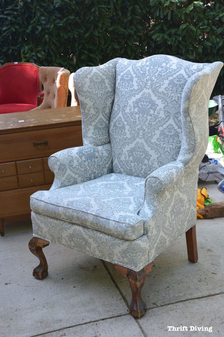 a blue and white wingback chair sitting on top of a cement floor next to a wooden dresser