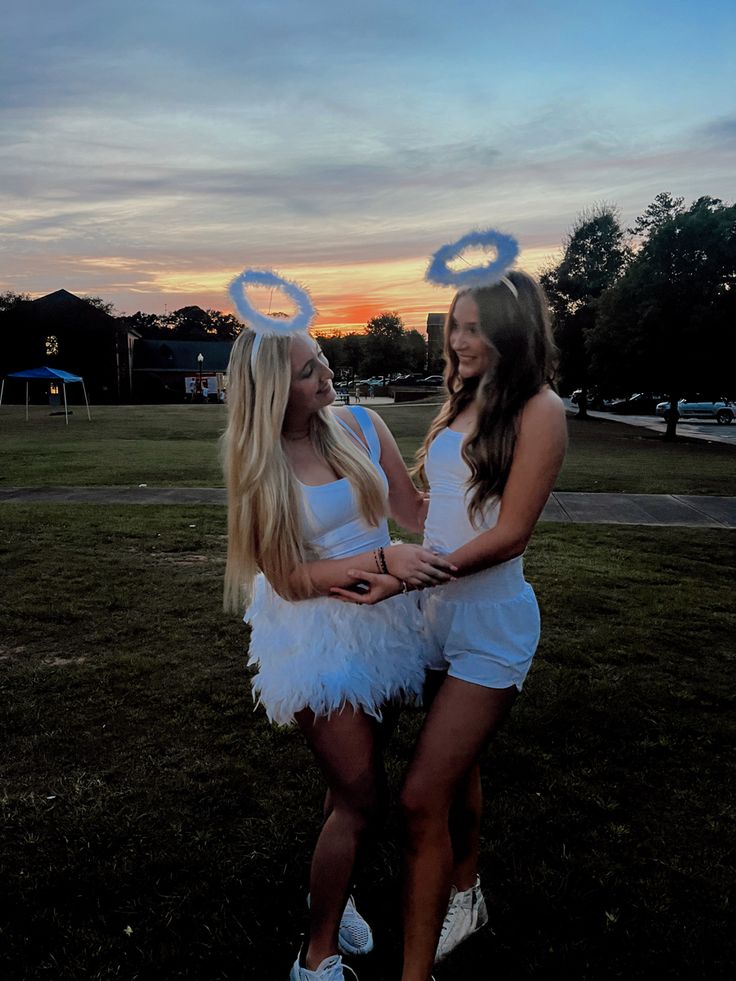 two beautiful young women standing next to each other on top of a grass covered field