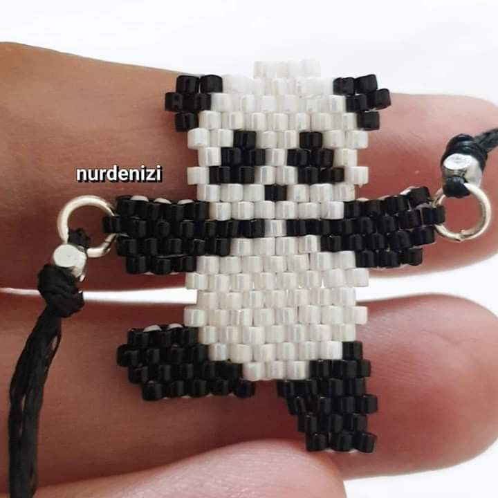 a hand holding a black and white beaded bracelet with a panda bear on it