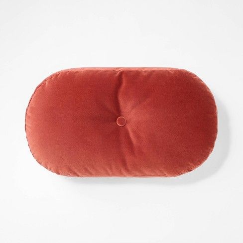 an orange round pillow on a white surface with a button in the middle and a small hole at the bottom