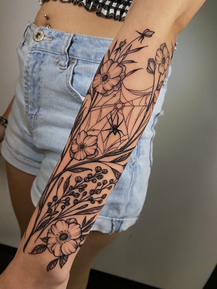 a woman's arm with flowers and leaves on it, in front of her