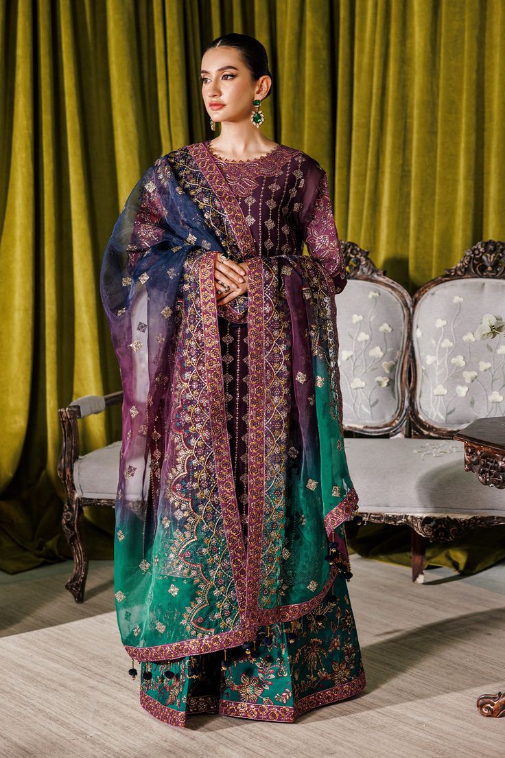 a woman standing in front of a couch wearing a purple and green dress with sheer sleeves