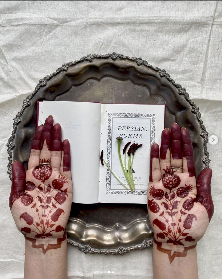 two hands with hendi designs on their palms holding a book