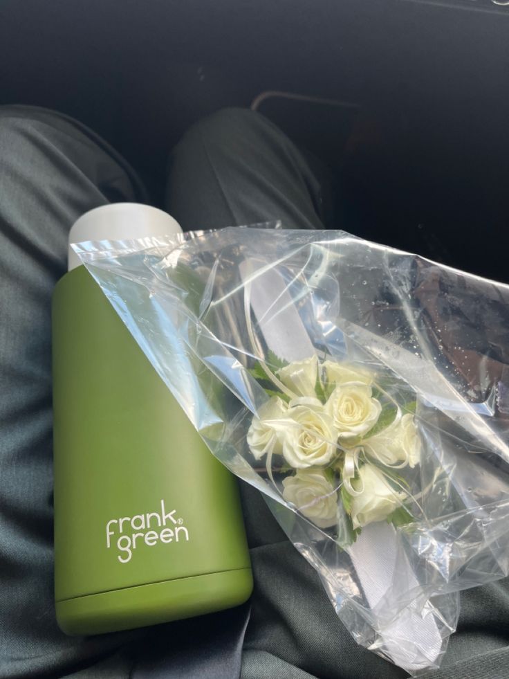 a bouquet of white roses sits on the back seat of a car next to a travel mug