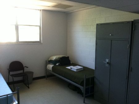 an empty room with two lockers and a single bed in the corner next to a chair