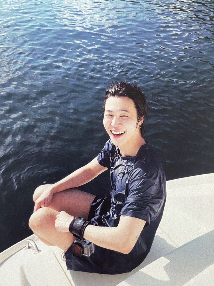 a young man sitting on top of a boat in the middle of the water smiling