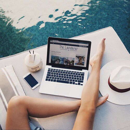 a person sitting at a table with a laptop and hat on top of it next to the water