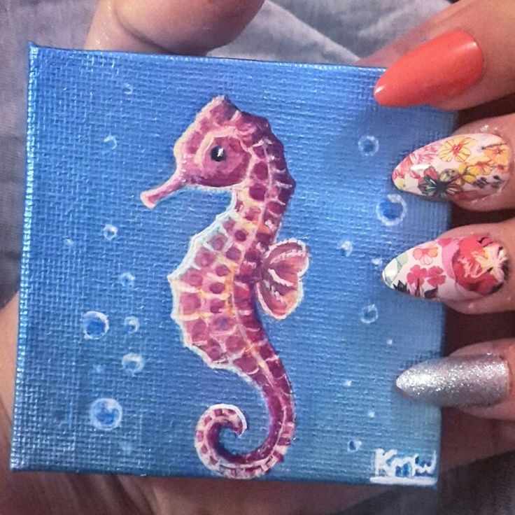 a woman's hand holding up a blue box with a painting of a sea horse on it