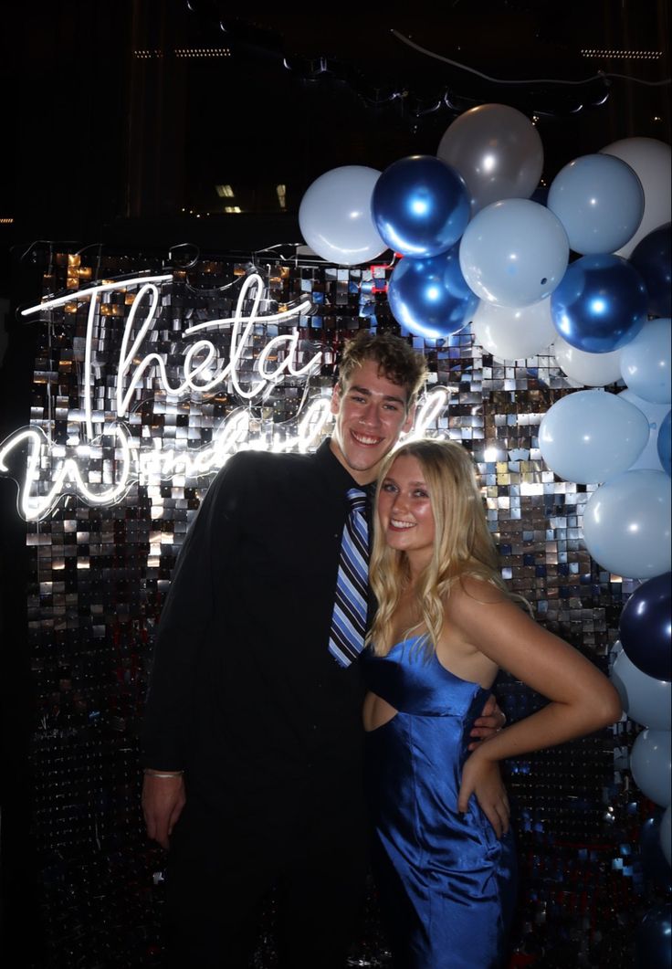 a man and woman posing for a photo in front of balloons that spell out the word theatre