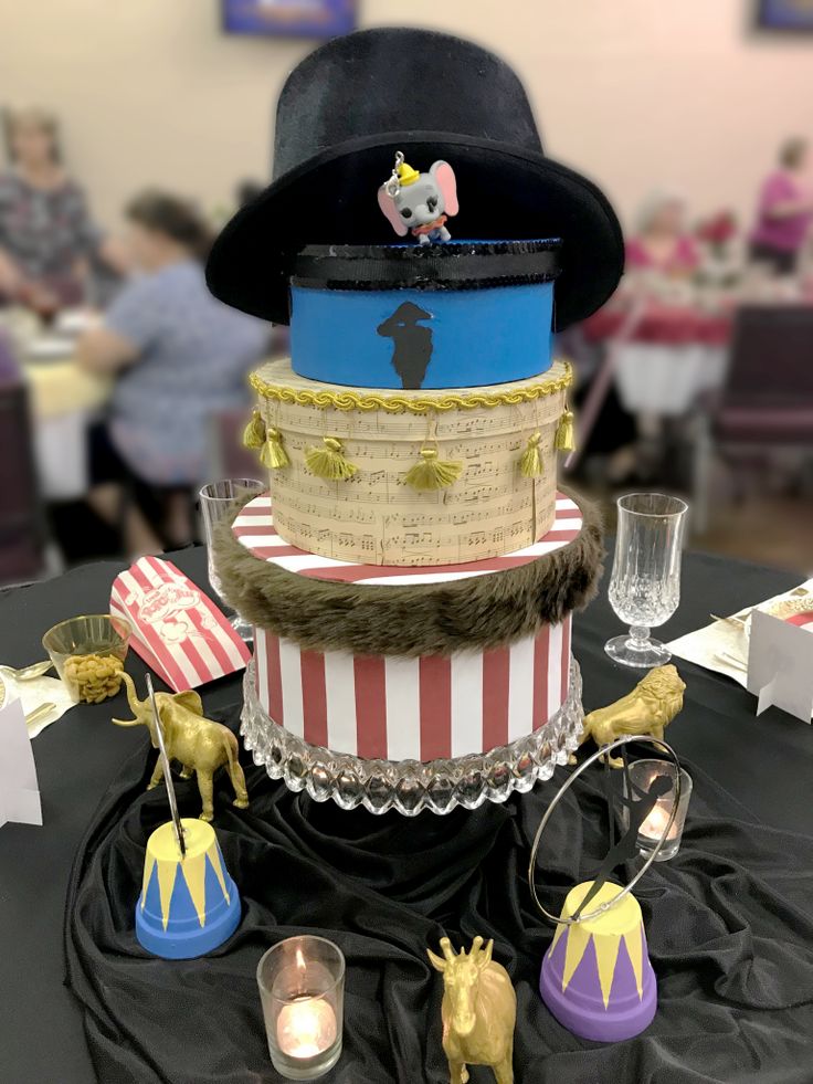 a three tiered cake with circus themed decorations on the top and sides, sitting on a black table cloth