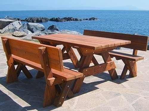 a wooden picnic table sitting on top of a stone covered ground next to the ocean