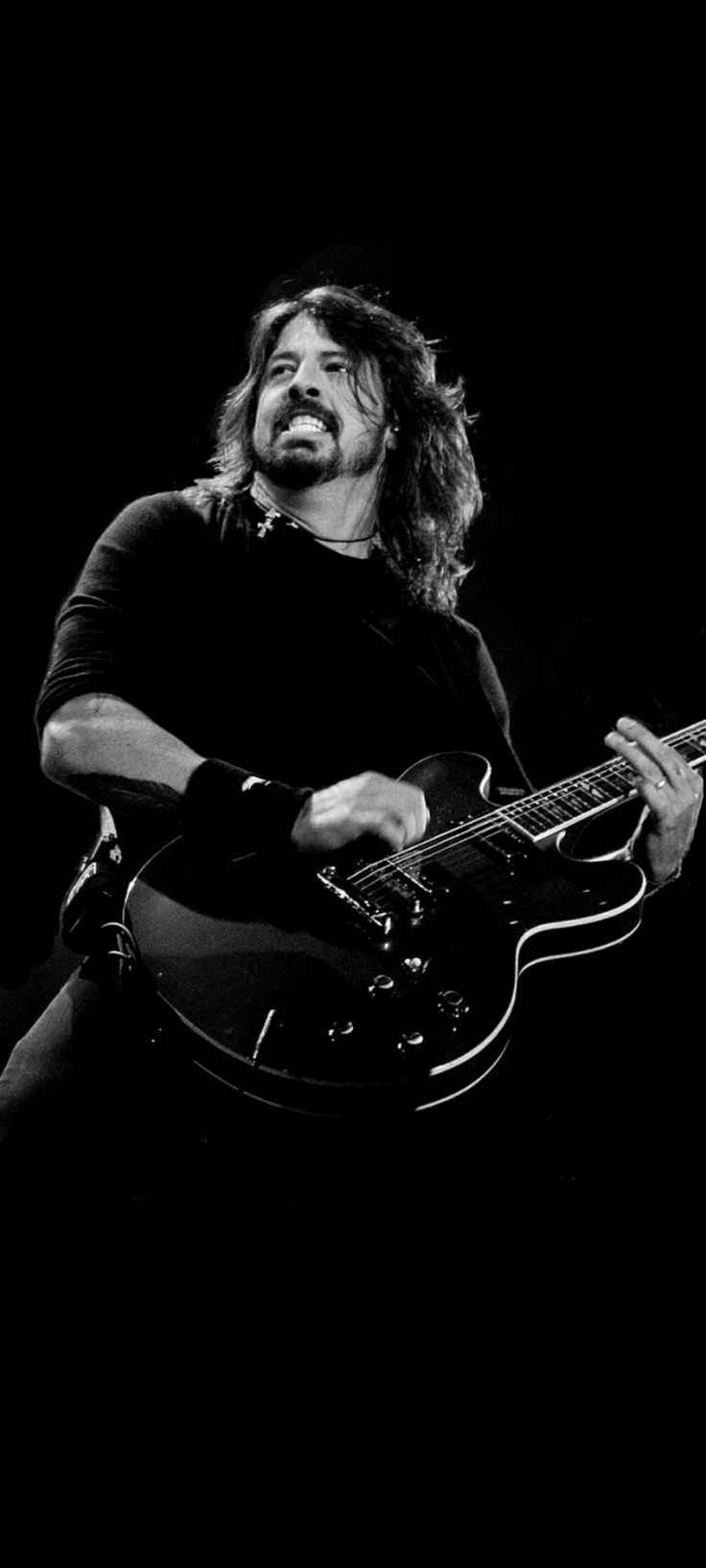 a man with long hair playing an electric guitar in black and white, against a dark background