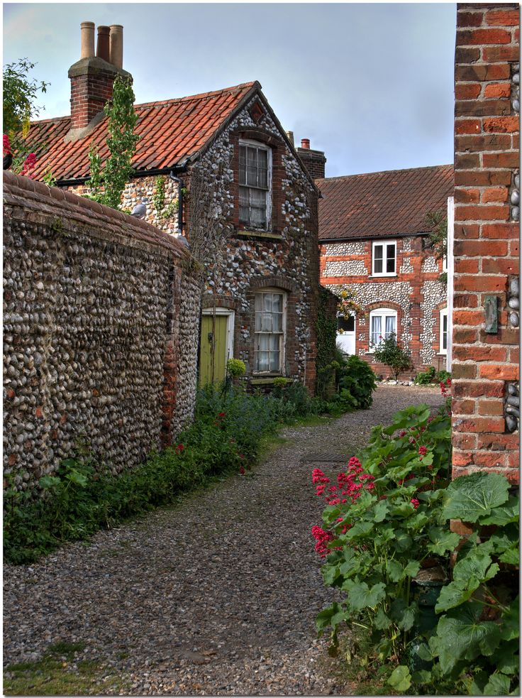 an old brick building with flowers growing in the front yard and walkway leading up to it