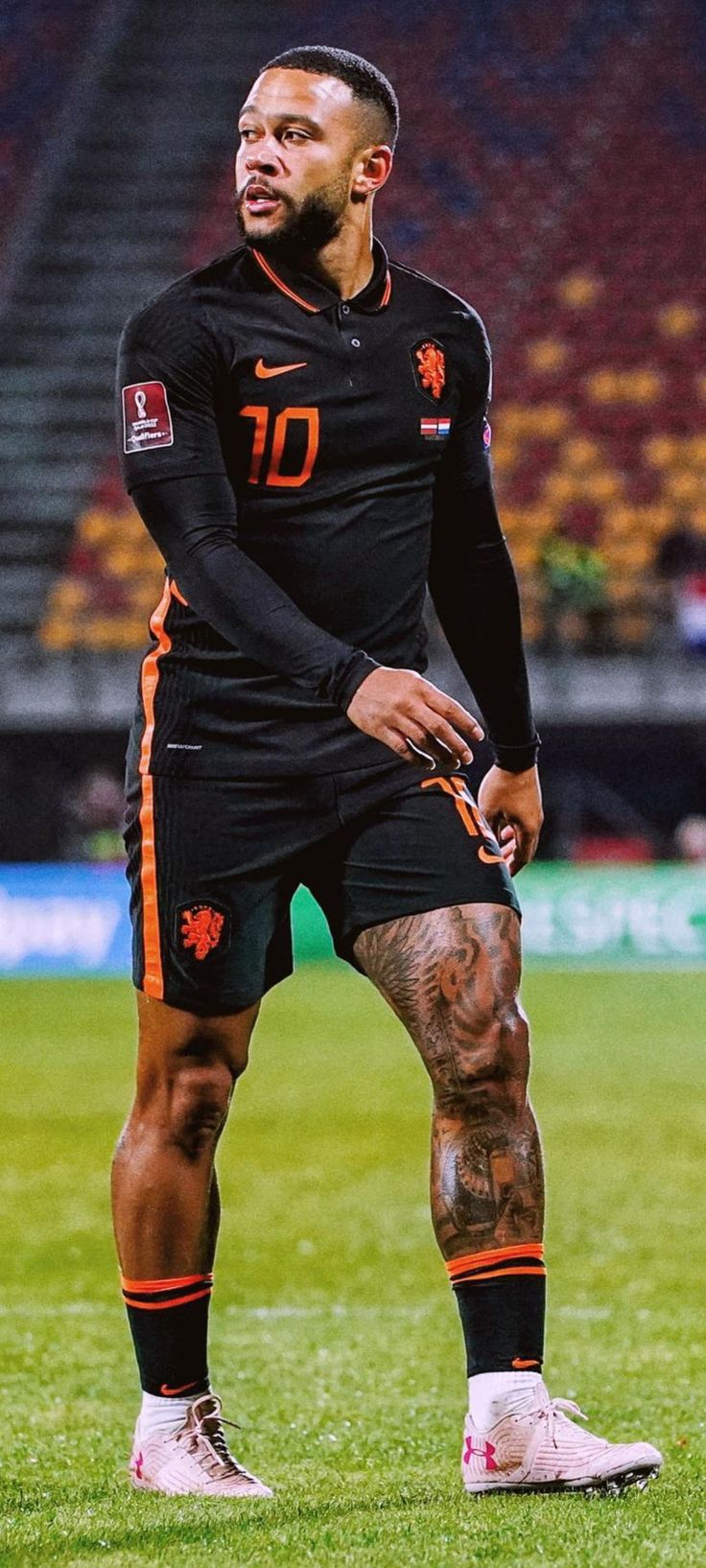 a man standing on top of a soccer field wearing black and orange uniforms with tattoos