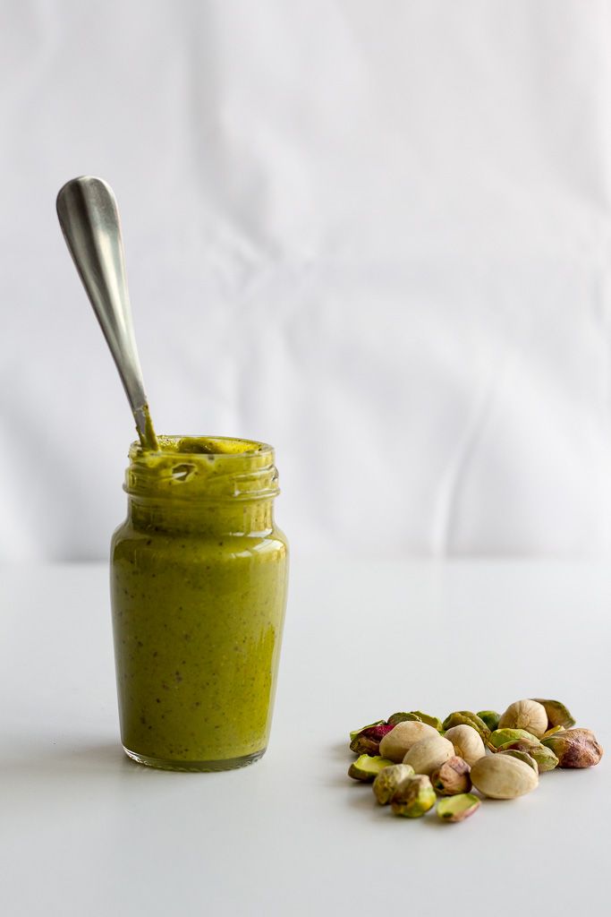 a jar filled with green smoothie next to nuts and a spoon on the table