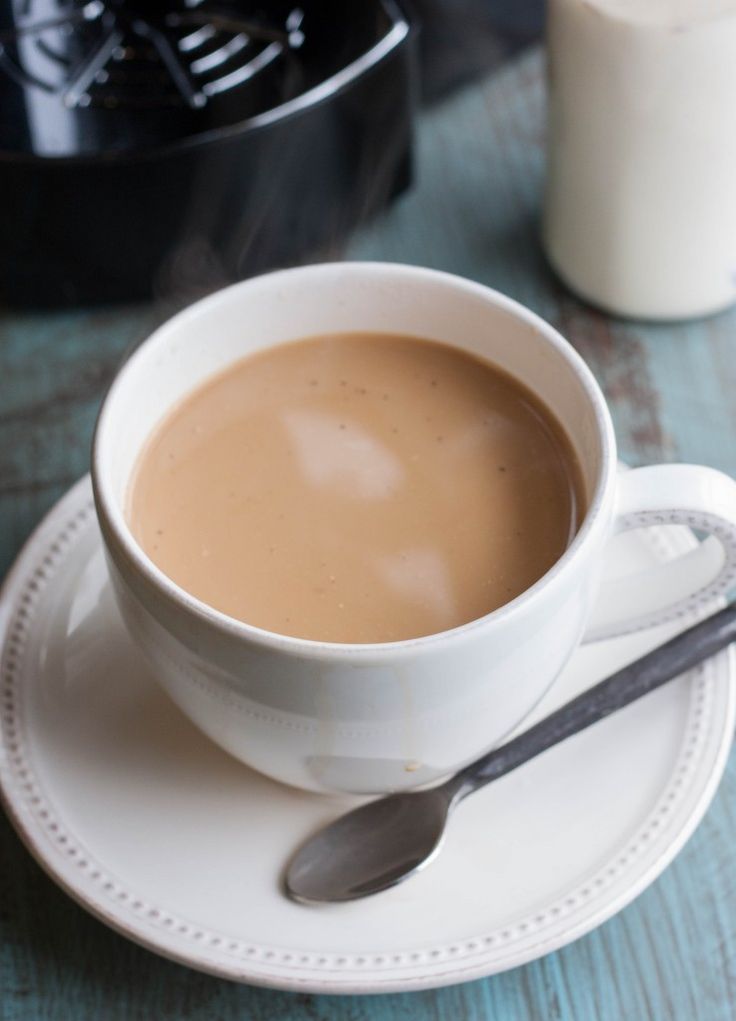 a cup of coffee sitting on top of a white saucer next to a black crock pot