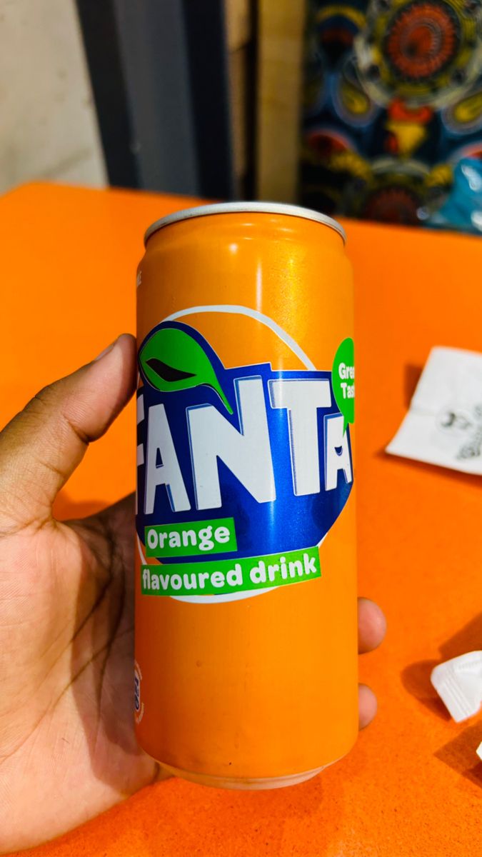 an orange beverage is being held up by someone's hand on an orange table