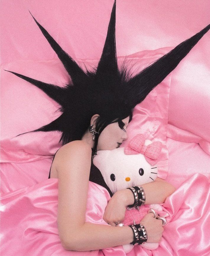 a woman laying on top of a pink bed next to a hello kitty stuffed animal