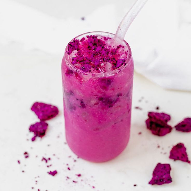 a glass filled with purple liquid sitting on top of a white table next to pink petals