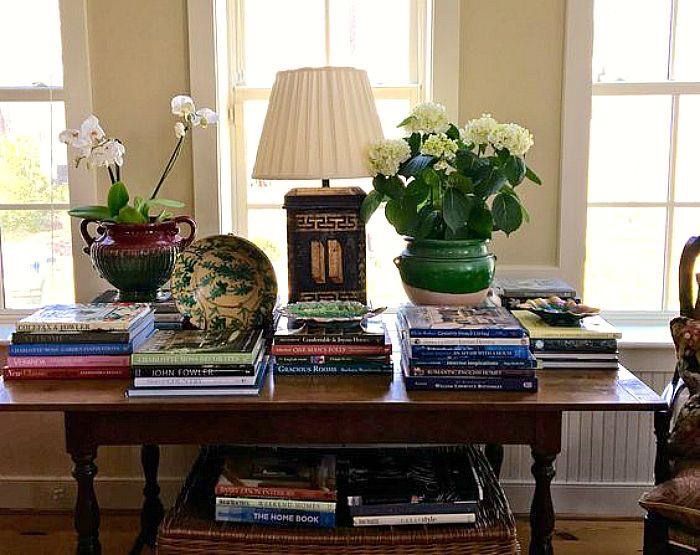 a table topped with books and vases filled with flowers next to a lamp on top of a wooden table