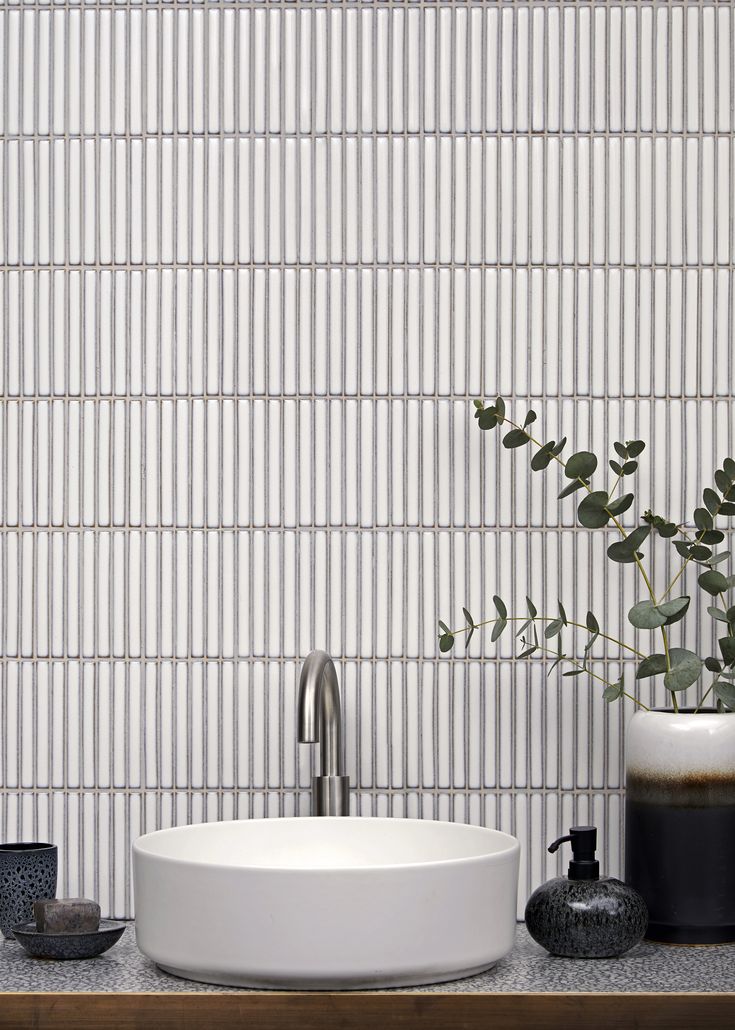 a white sink sitting on top of a wooden counter next to a vase with green leaves