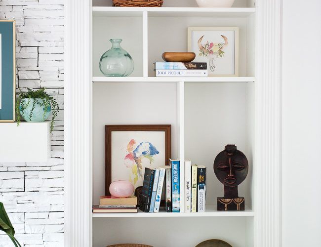 a bookshelf filled with lots of books next to a potted plant and pictures