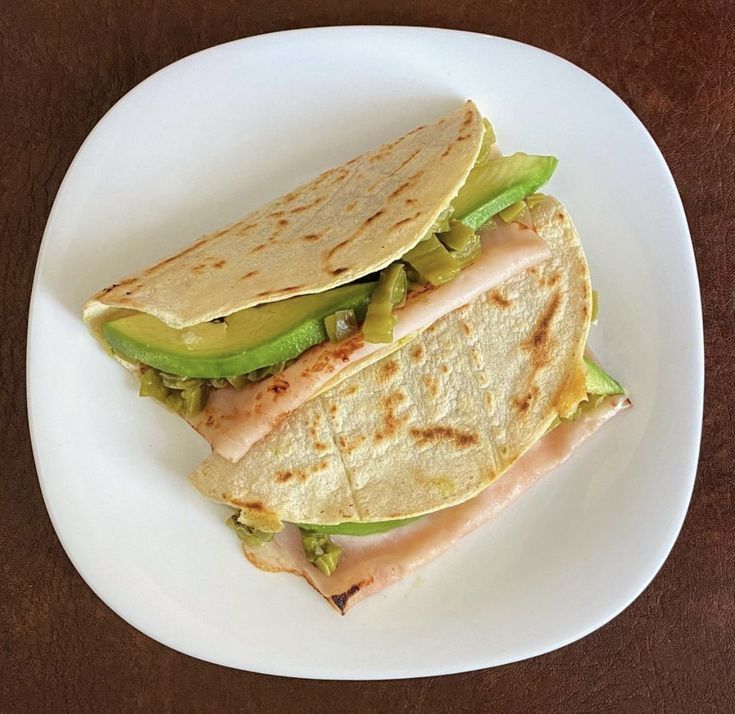 a white plate topped with two quesadillas and an avocado slice