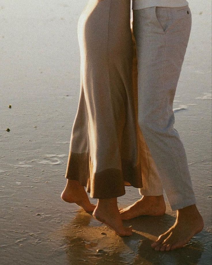 two people standing on the beach hugging each other