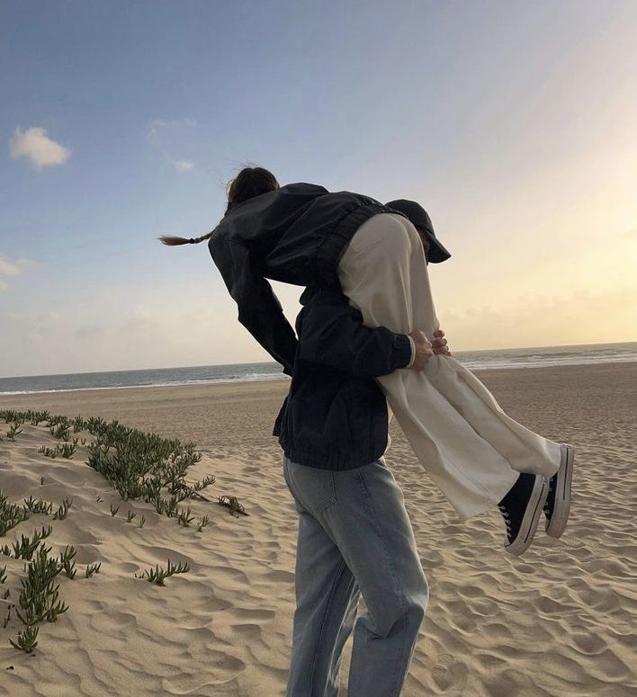 a man carrying a woman on his back while walking along the sand at the beach