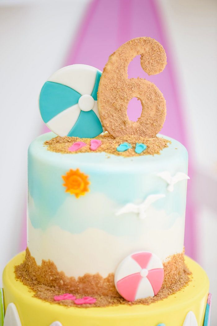 there is a cake that has the number six on it and beach balls in the sand