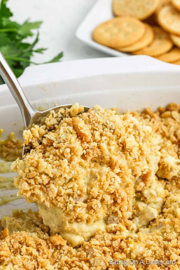 a close up of a spoon in a casserole dish with crackers on the side