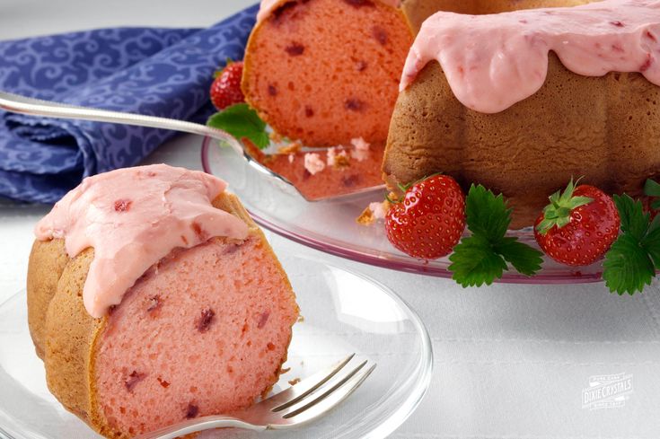 a bundt cake with pink icing and strawberries on the plate next to it