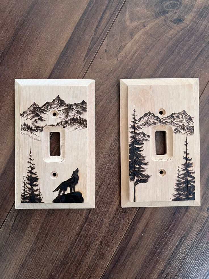 two wooden switchplates decorated with mountains and a wolf